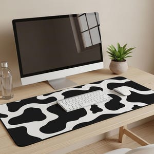 May include: A black and white cow print desk mat with a computer, keyboard, and mouse on a wooden desk. A small potted plant sits to the right of the computer. A water bottle and pencils are to the left of the computer.