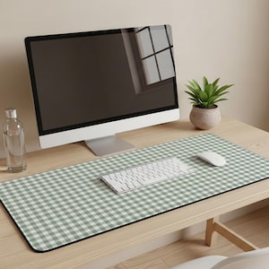 May include: A desk setup featuring a computer monitor, keyboard, and mouse on a wooden desk. A large rectangular desk mat with a green and white gingham pattern covers the desk surface. A small potted plant and a water bottle are also visible.