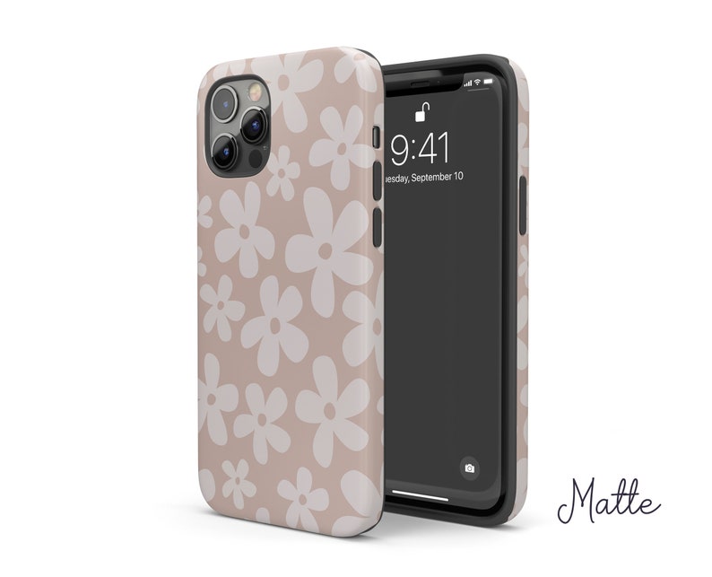 May include: A beige phone case with a white daisy pattern. The case is made of a matte material and has a clear back. The phone case is compatible with iPhone models.