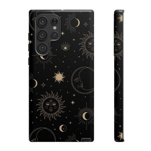 May include: A black phone case with a gold celestial pattern featuring suns, moons, and stars. The case has a cutout for the phone's camera.