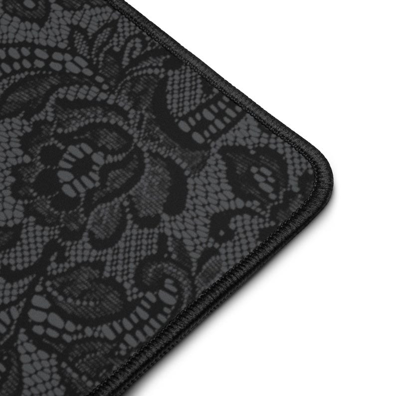May include: A black and gray mousepad featuring a detailed lace pattern. The edges are finished with black stitching. The design is a close-up of the lace, showing the intricate floral and geometric details.