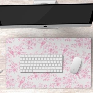 May include: A white desk mat with a pink floral pattern and pink birds. The mat is on a white wooden desk with a computer monitor, keyboard, and mouse.