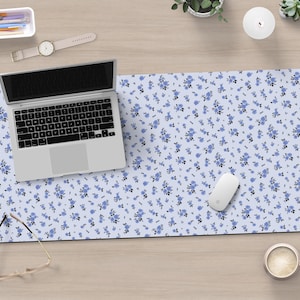 May include: A blue and white floral patterned desk mat with a laptop, a computer mouse, a pair of glasses, and a cup of coffee on top of it.