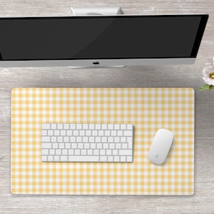 May include: A yellow and white gingham desk mat with a white keyboard and mouse on top. The desk mat is on a light wood surface.