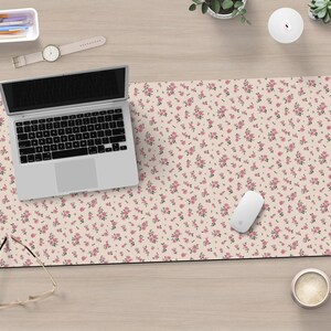 K&ouml;nnte beinhalten: Eine hellrosa Schreibtischmatte mit einem kleinen rosa Blumenmuster. Ein Laptop, eine Maus, eine Brille, eine Tasse Kaffee und eine Uhr liegen auf der Schreibtischmatte.