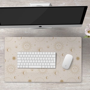 May include: A beige desk mat with a gold celestial pattern featuring suns, moons, and stars. A white keyboard and mouse are placed on the mat.