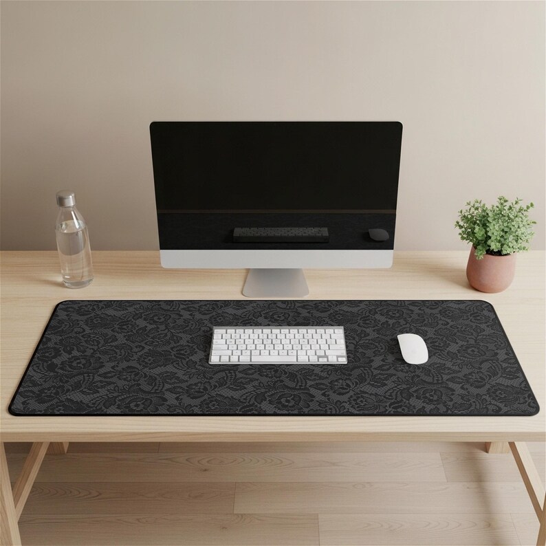 May include: A black floral patterned desk mat with a white keyboard and mouse. A large computer monitor, a water bottle, and a small potted plant are also on the wooden desk.