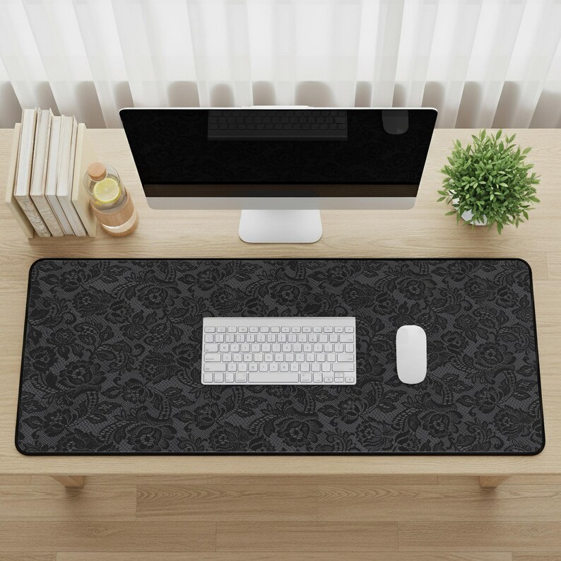 May include: A black floral patterned desk mat with a white keyboard and mouse. A computer monitor, books, and a small plant are also on the wooden desk. The desk mat measures approximately 31.5 inches long and 11.8 inches wide.