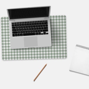 Pode incluir: Um computador port&aacute;til branco com um teclado preto est&aacute; em uma esteira de mesa quadriculada verde e branca. Um caderno branco em espiral e um l&aacute;pis marrom est&atilde;o na superf&iacute;cie branca.