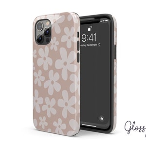 May include: A beige phone case with a white daisy pattern. The case is designed for an iPhone with a camera bump. The phone case is glossy.