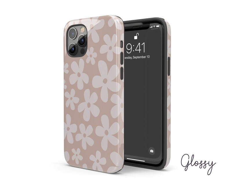 May include: A beige phone case with a white daisy pattern. The case is designed for an iPhone with a camera bump. The phone case is glossy.