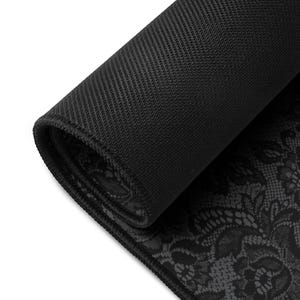 May include: A rolled-up black mouse pad with a textured, non-slip backing. The top surface features a detailed, dark gray lace pattern. The edges are neatly finished with a black border, providing a clean and elegant look.