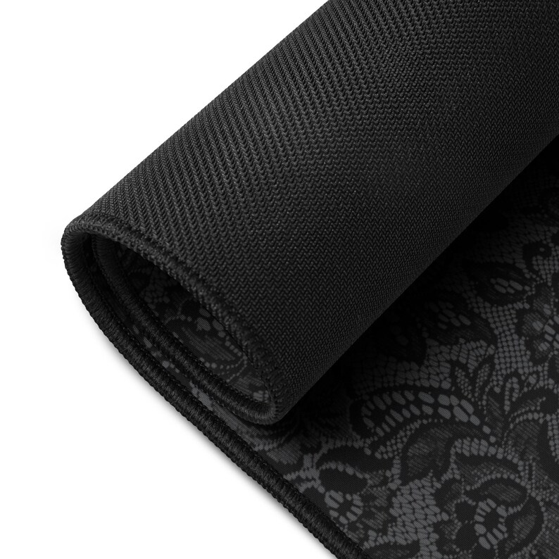 May include: A rolled-up black mouse pad with a textured, non-slip backing. The top surface features a detailed, dark gray lace pattern. The edges are neatly finished with a black border, providing a clean and elegant look.