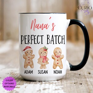 May include: White ceramic mug with a black handle and rim. The mug features the text "Nana's PERFECT BATCH" in red and black, with illustrations of gingerbread people named Adam, Susan, and Noah. "Color Options Available" is also visible.
