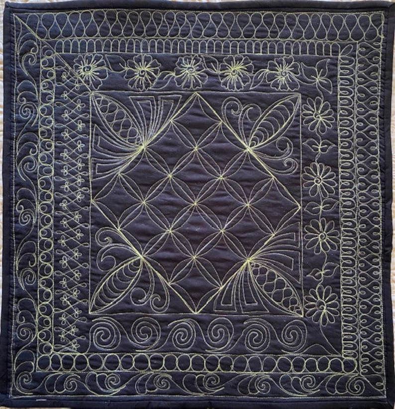 May include: A dark blue quilted fabric with a geometric pattern stitched in a light yellow thread. The fabric has a border of various decorative stitches.