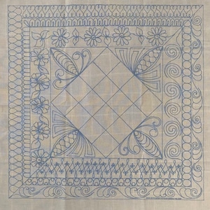 May include: A white fabric with a blue design of a square with a diamond pattern inside. The square is surrounded by a border of floral and swirl designs. The fabric is marked with the text "www.stitcherydesigns.com/free.trial"