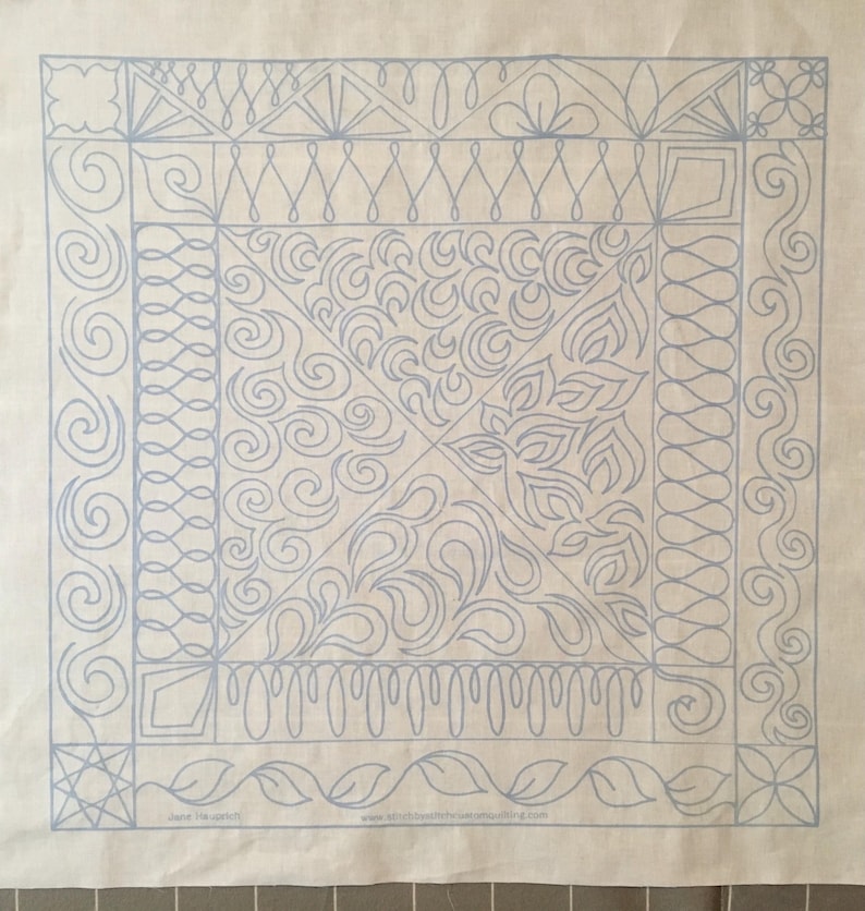 May include: A white fabric square with a blue outline of a quilt pattern. The pattern includes a variety of swirls, leaves, and geometric shapes.