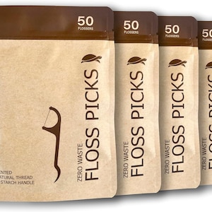 May include: Four brown pouches of 50 compostable floss picks each. The pouches are labeled "Zero Waste Floss Picks" and feature a turtle logo. The text "50 Flossers" is printed on the top of each pouch. The pouches are made of brown paper and have a white background.