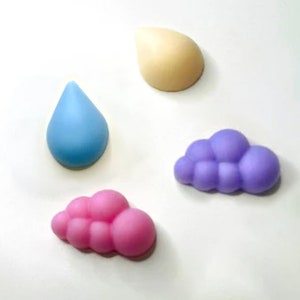 Puede incluir: Cuatro formas de jabón de colores: una gota de lluvia azul claro, una gota de lluvia amarilla clara, una nube morada clara y una nube rosa clara.