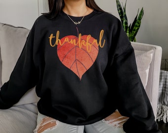 May include: Black sweatshirt featuring a large orange and red leaf design with the word "thankful" in gold lettering.