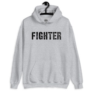 May include: A gray hooded sweatshirt with the word "FIGHTER" printed in black on the front. The text has a distressed, vintage look.