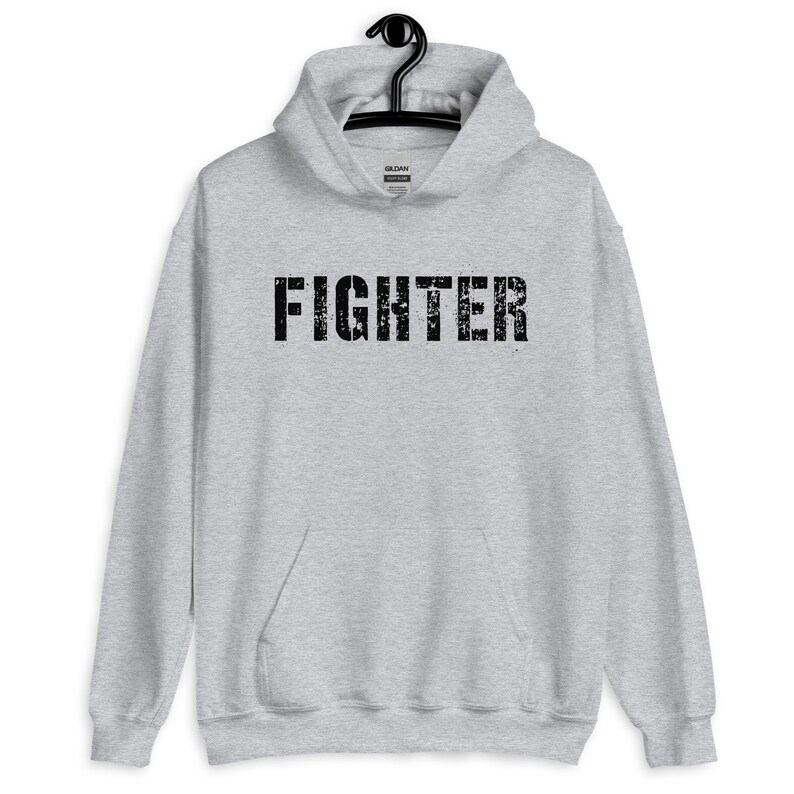 May include: A gray hooded sweatshirt with the word "FIGHTER" printed in black on the front. The text has a distressed, vintage look.