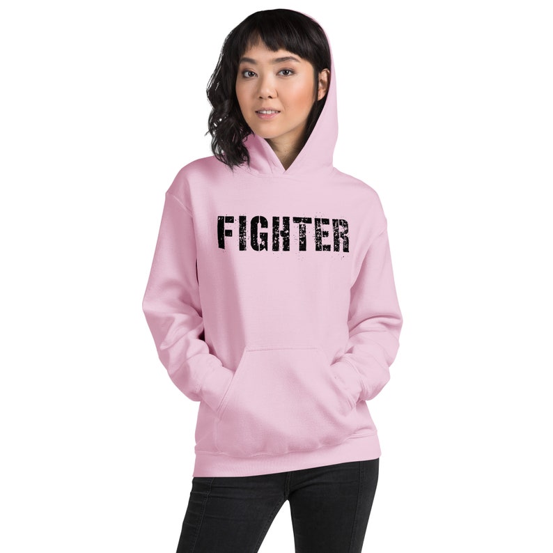 May include: A pink hoodie with a black distressed text graphic that says "FIGHTER".