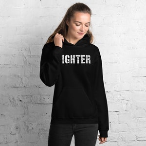May include: Black hooded sweatshirt with the word "FIGHTER" printed in white on the front.