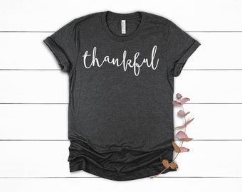 Puede incluir: Una camiseta gris oscuro con la palabra "thankful" escrita en letras blancas cursivas.