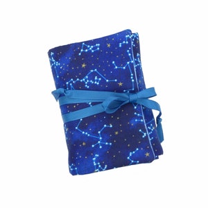 May include: A blue fabric pouch with a constellation pattern and gold stars. The pouch is tied with a blue ribbon.