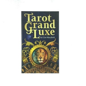 May include: A Tarot Grand Luxe deck by Ciro Marchetti. The cover features the title in gold lettering against a dark blue background with a starry design. A central image shows a lion's face within a golden gear, with clock-like details.