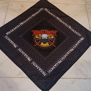 May include: Black bandana featuring the band Megadeth's logo in the center, a skull with lightning bolts and the band's name. The band's name is also printed around the border in white. The bandana has a geometric pattern.