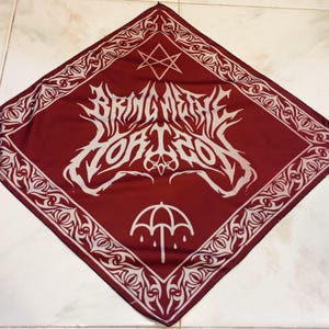 May include: A square bandana in deep red featuring a white border with intricate tribal patterns. The center displays the white text "BRING ME THE HORIZON" in a stylized font, a geometric star symbol above, and an umbrella icon with raindrops below.