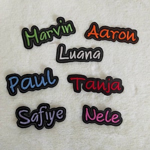 Könnte beinhalten: Acht gestickte Bügelbilder mit verschiedenen Namen. Die Namen sind: Harvin, Aaron, Luana, Paul, Tanja, Safiye und Nele.