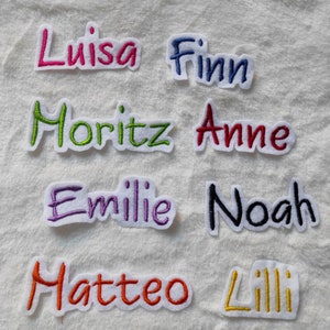 Könnte beinhalten: Acht gestickte Stoffpatches mit verschiedenen Namen, darunter Luisa, Finn, Moritz, Anne, Emilie, Noah, Matteo und Lilli. Die Patches befinden sich auf einem weißen Hintergrund.