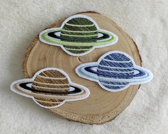 May include: Three embroidered iron-on patches of Saturn, each with a different color ring: green, blue, and brown.
