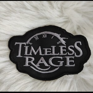 Könnte beinhalten: Schwarzer und weißer gestickter Aufnäher mit den Worten "Timeless Rage" und einem Zifferblattmuster.