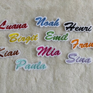 Könnte beinhalten: Eine Sammlung von 10 bunten gestickten Bügelbildern mit Namen wie Luana, Noah, Henri, Birgit, Emil, Franz, Kian, Mia, Paula und Sina.