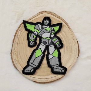 Könnte beinhalten: Grün-grauer gestickter Bügelaufkleber mit einem Roboter mit einem Stern auf der Brust.
