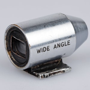 Puede incluir: Un objetivo gran angular plateado para c&aacute;mara. El cuerpo cil&iacute;ndrico de metal tiene las palabras "WIDE ANGLE" impresas en el lateral. La lente tiene una abertura cuadrada y una peque&ntilde;a base rectangular.