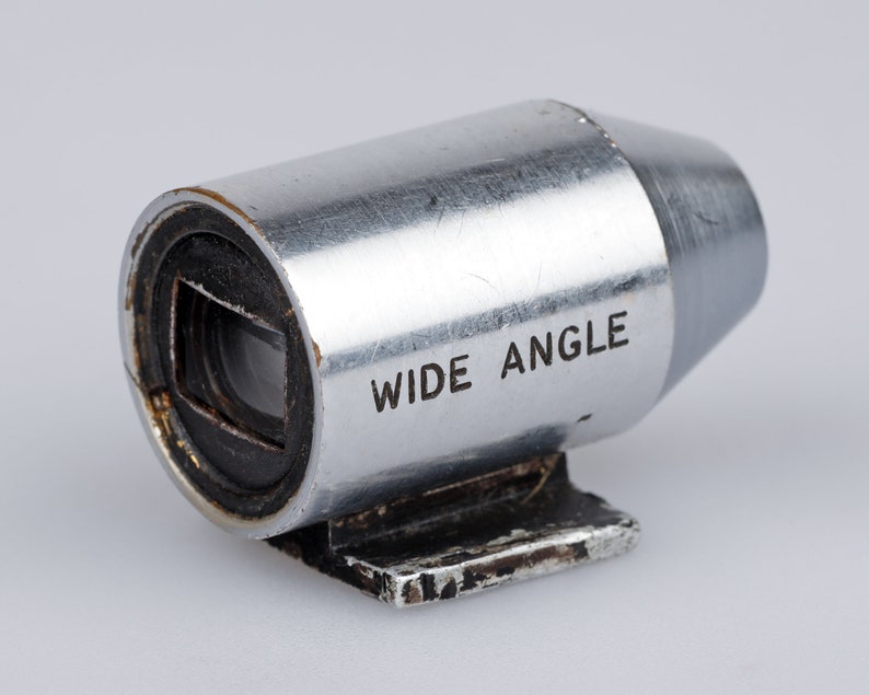 Puede incluir: Un objetivo gran angular plateado para c&aacute;mara. El cuerpo cil&iacute;ndrico de metal tiene las palabras "WIDE ANGLE" impresas en el lateral. La lente tiene una abertura cuadrada y una peque&ntilde;a base rectangular.