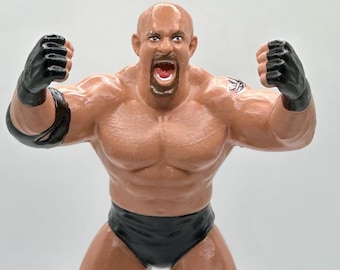 May include: A black and brown action figure of a wrestler with a bald head, black knee pads, black boots, and a black wrestling outfit. The figure is posed with its arms raised in a triumphant gesture.