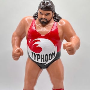 May include: A red, white, and black wrestling figure with the word "TYPHOON" on the front. The figure is wearing red boots with white laces.