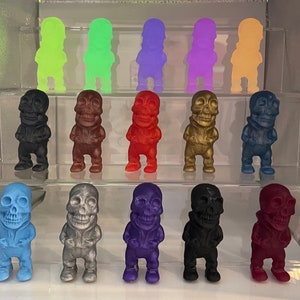 May include: Ten small skeleton figurines in various colors, including blue, green, purple, gold, red, and black. The skeletons are all wearing different outfits and have different poses.