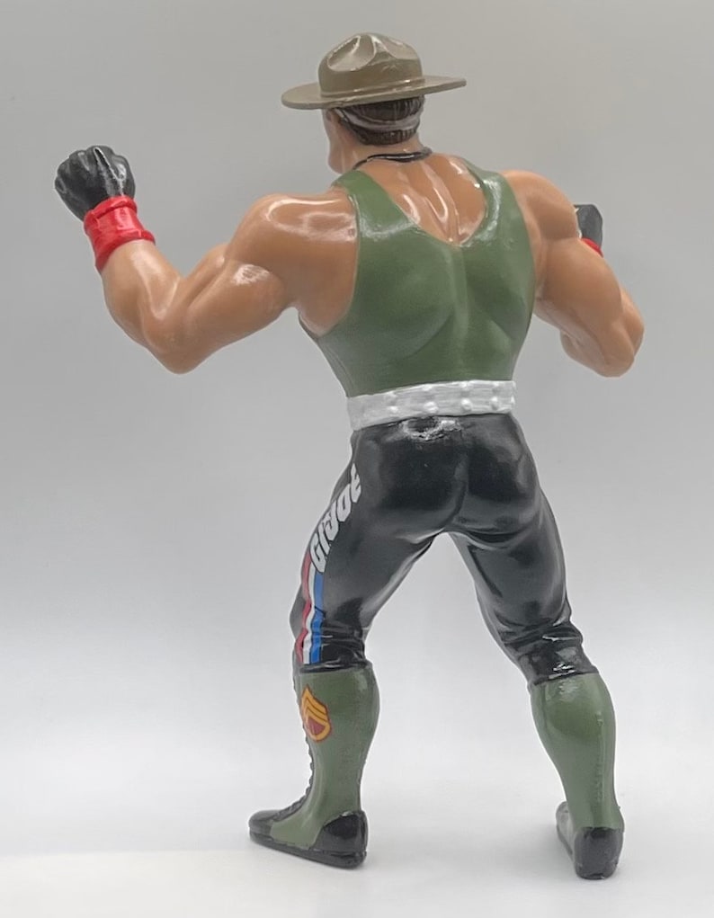 May include: A green and black action figure wearing a green tank top, black pants with a white stripe and a red, white, and blue stripe, and a green and black hat. The figure is holding its fists up in a fighting pose.