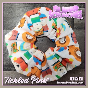以下が含まれることがあります： サウスパークのキャラクターが繰り返し描かれた白いスクランチー。スクランチーは布製で、白い背景にカラフルなキャラクターが描かれています。画像の右上には「Super Scrunchies」というテキストが、左下には「Tickled Pink」というテキストが書かれています。