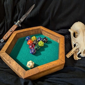 May include: A wooden hexagonal dice tray with a green felt interior.  The tray is filled with colorful dice with black numbers.  A small knife and a white animal skull are also in the image.