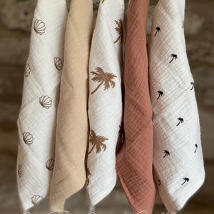 May include: Five hanging cloths in a range of colours and patterns. Two are white with seashell and palm tree designs, one is beige, and one is coral. The text "By The Beach Collection" is at the bottom.