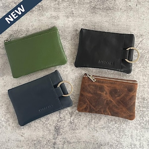 May include: Four leather coin purses in green, black, navy, and brown. The green and brown purses have a zipper closure. The black and navy purses have a metal ring. The word "SPROCKET" is embossed on the black and navy purses. A "NEW" banner is in the upper left corner.