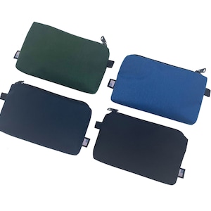 May include: Four zippered pouches in different colors: green, blue, black, and dark gray. Each pouch has a zipper closure and a small American flag patch.